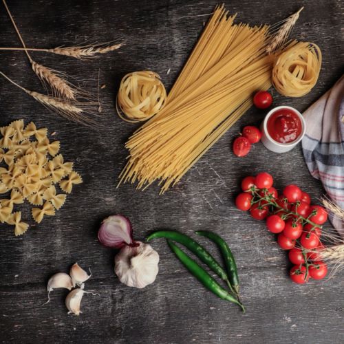 flatlay photo of pasta noodles, tomatoes, tomato sauce, onions, and garlic